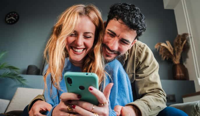 A smiling couple joyfully looks at a smartphone screen together.