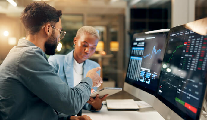 One man explaining to a woman information on a tablet with too large screens in front of them showing data tables and charts.