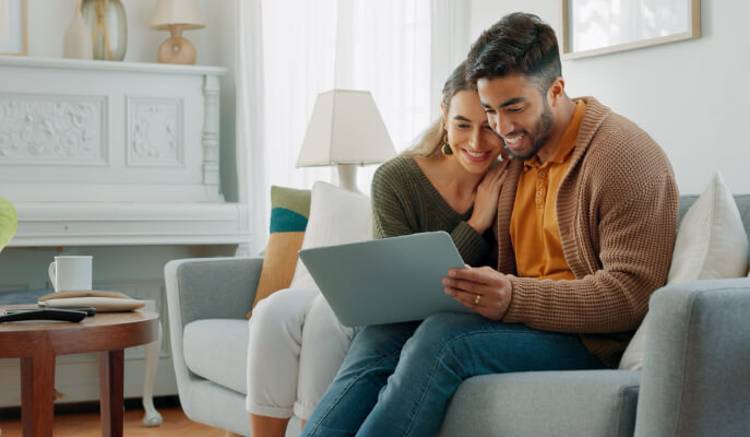 Smiling couple sitting together on a cozy living room sofa, looking at a laptop and planning finances or investments.