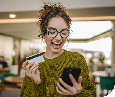 Happy woman looking at phone and holding credit card in other hand.
