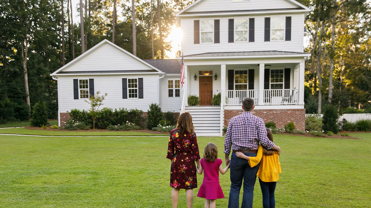 Family of four standing in front yard looking at new home.