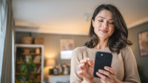 Woman standing in living room looking at cell phone.